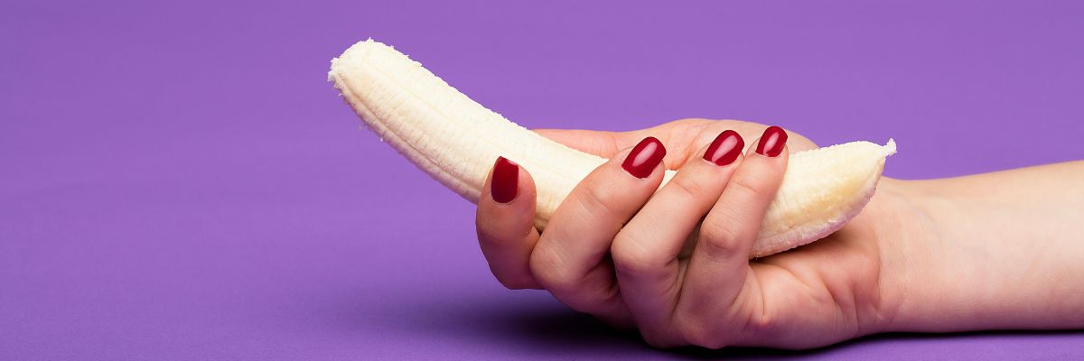 hand met rode nagellak houdt een banaan vast op een paarse achtergrond 