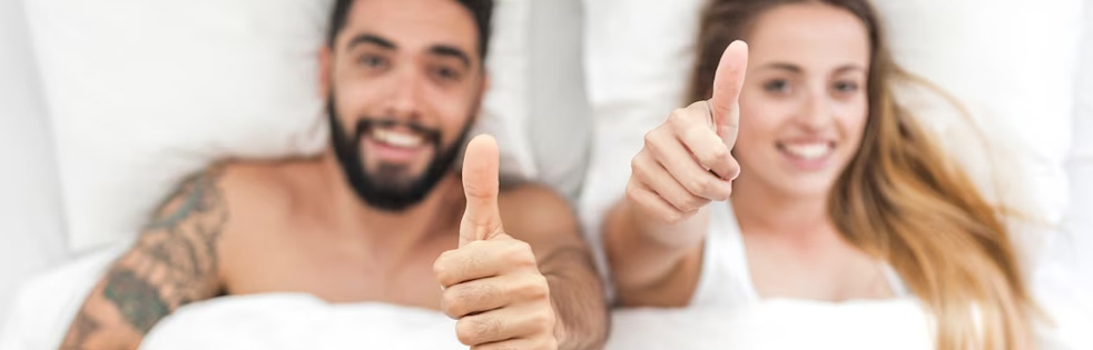 twee mensen liggen samen in bed en steken duim op