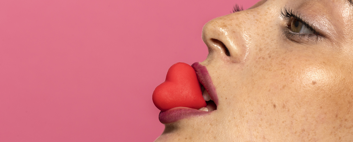 vrouw houdt een rood hartjessnoepje tussen haar lippen
