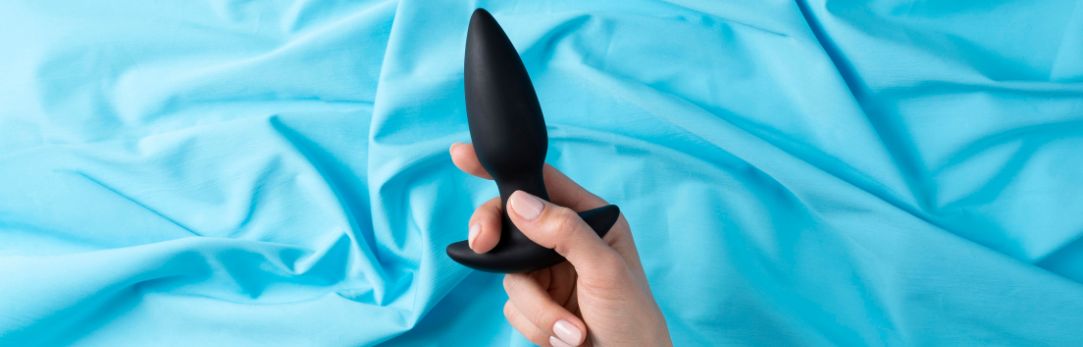 vrouw-houdt-een-zwarte-buttplugs-vast-boven-een-blauwe-deken